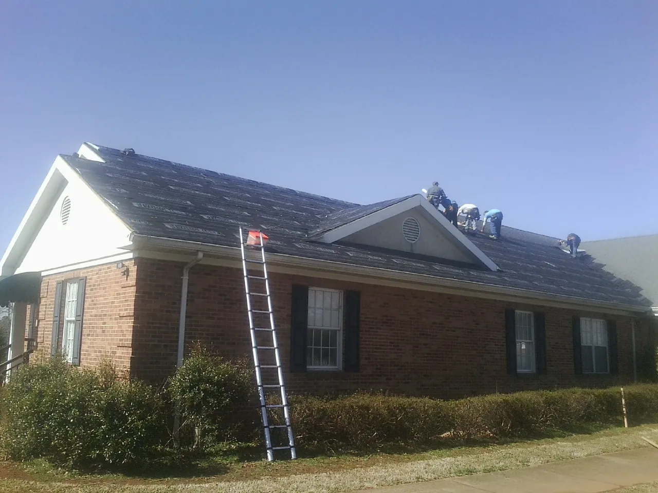 Crew tearing shingles off a brick ranch roof with a ladder set — Metal Roof Repair work by our crew in Laveen