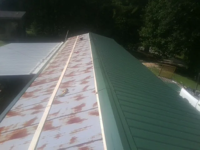 Old rusted panels beside newly installed green metal roofing — Wind Damage Roof Repair by Roofing Brothers in Laveen