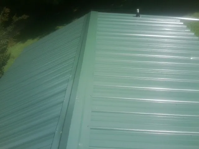 New green metal panels meeting at the ridge of a roof — Flat Roof Repair work by our crew in Laveen