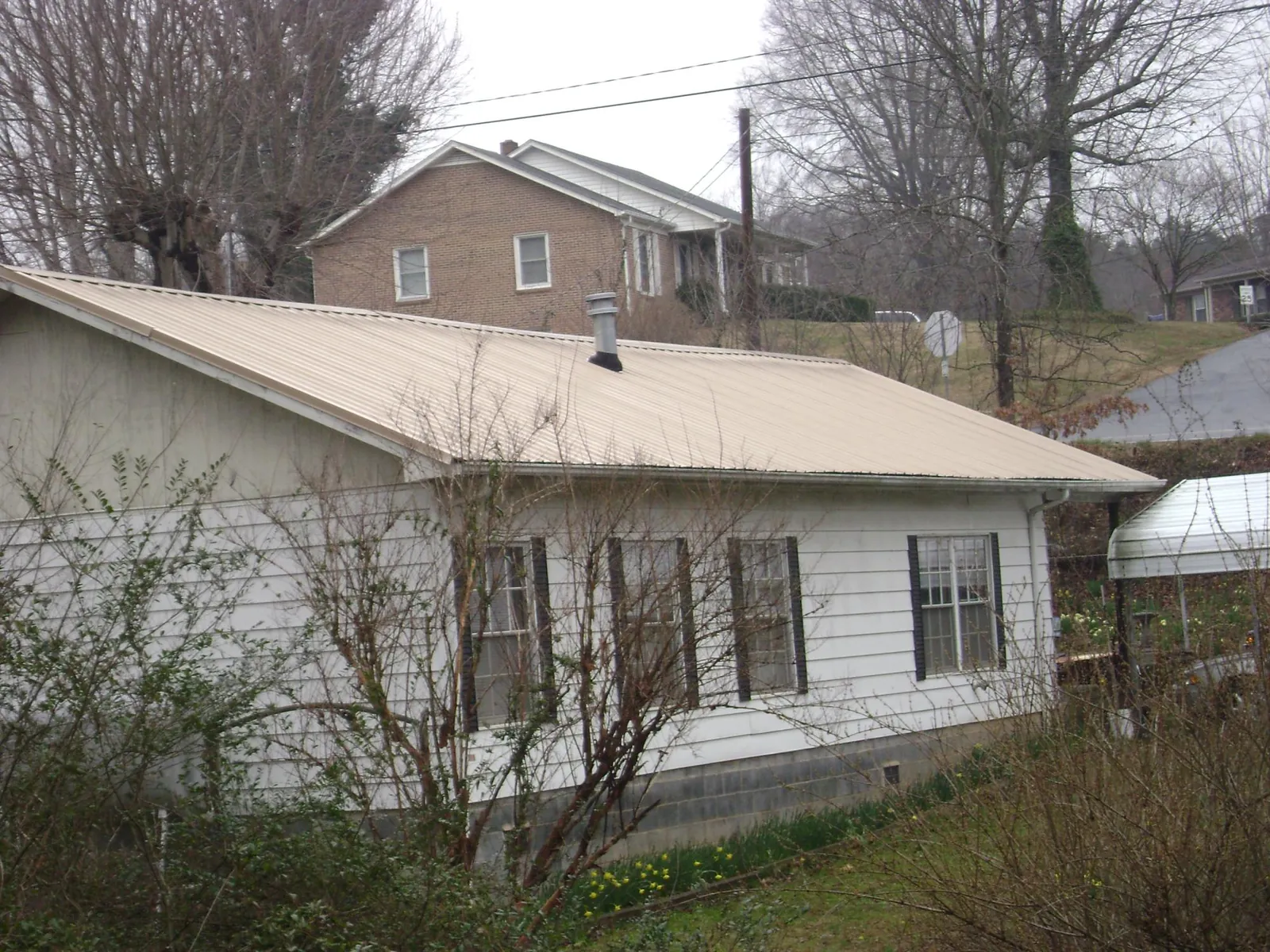 Tan metal roof on a white sided house set into a hillside — Commercial Roofing by Roofing Brothers in Laveen