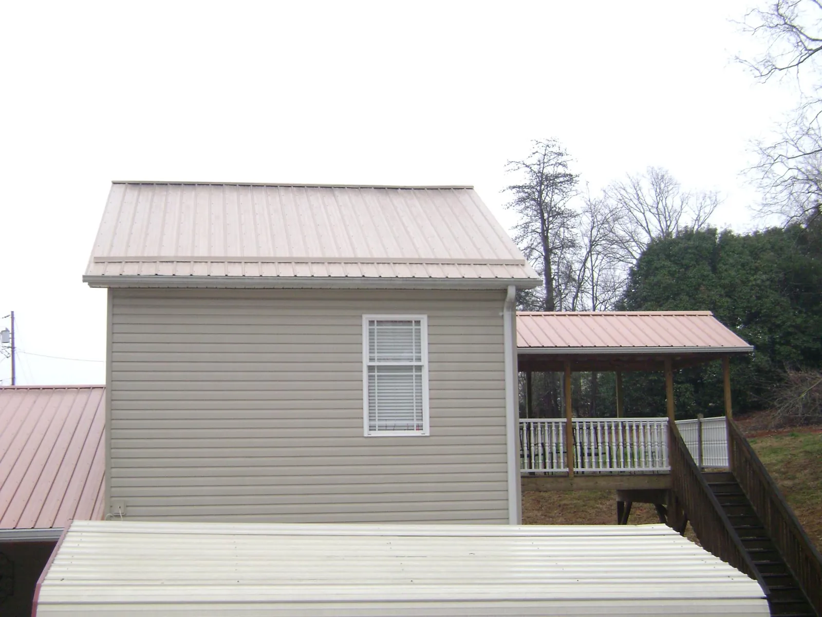 Tan metal roofs on a two story addition and attached porch, from a Roof Replacement job in Laveen
